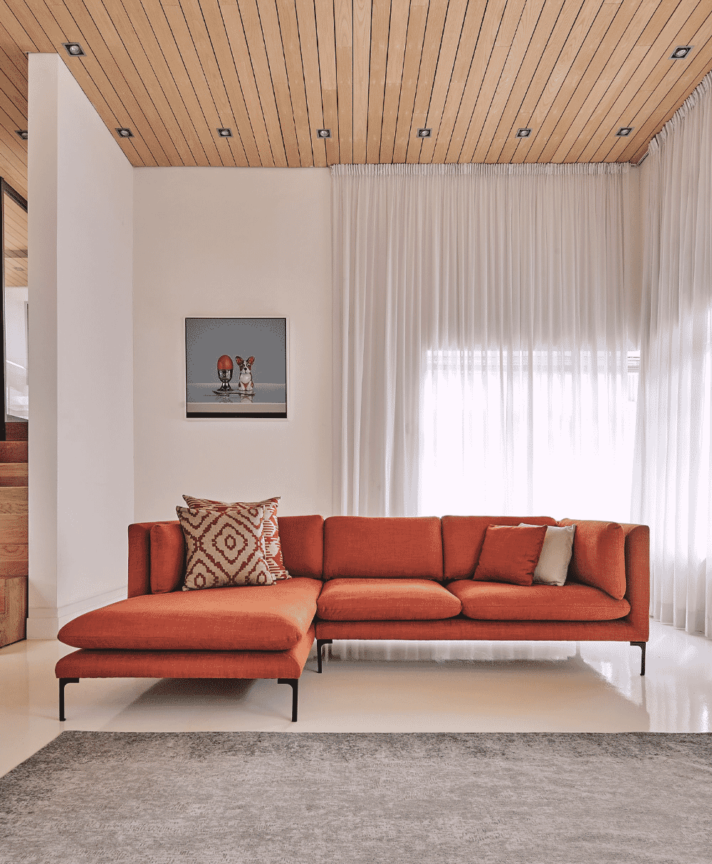 Orange sectional sofa against white walls and a wooden ceiling with soft natural light.