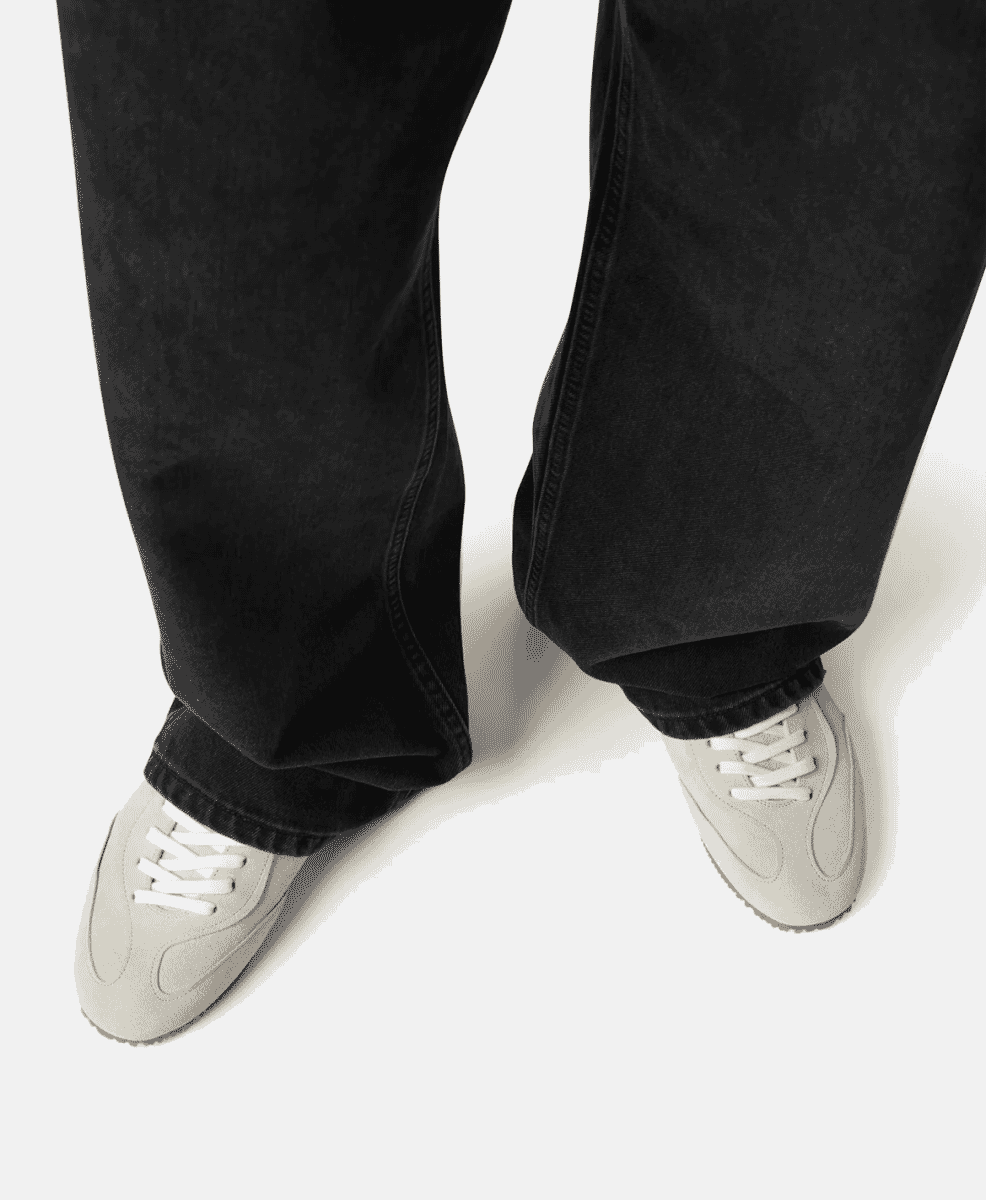Top-down view of wide-leg black denim paired with beige slim sneakers.
