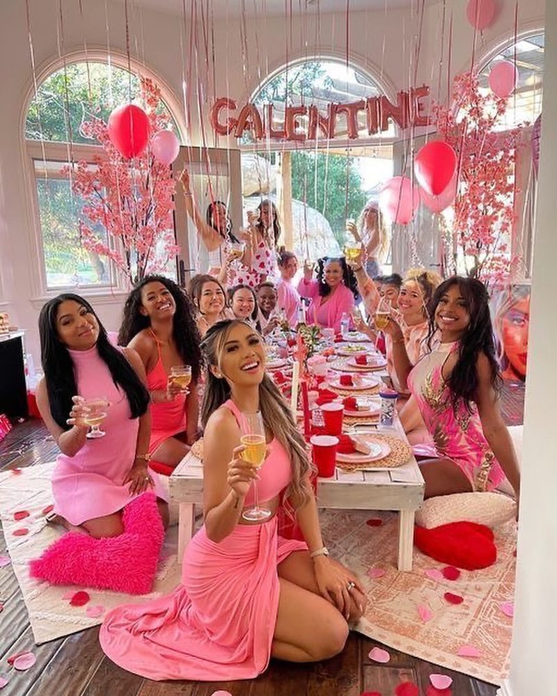 Women in coordinated pink fashion sitting at a festive brunch table with rose petals and balloons.