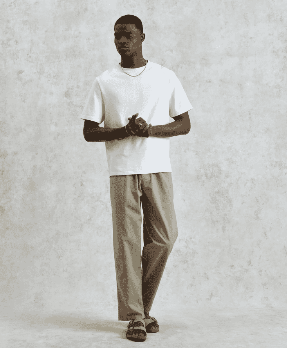 Man in light khaki relaxed-fit trousers and sandals against a neutral backdrop.