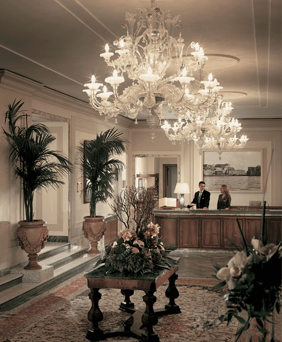 Professional hotel staff in formal attire standing behind an ornate reception desk.
