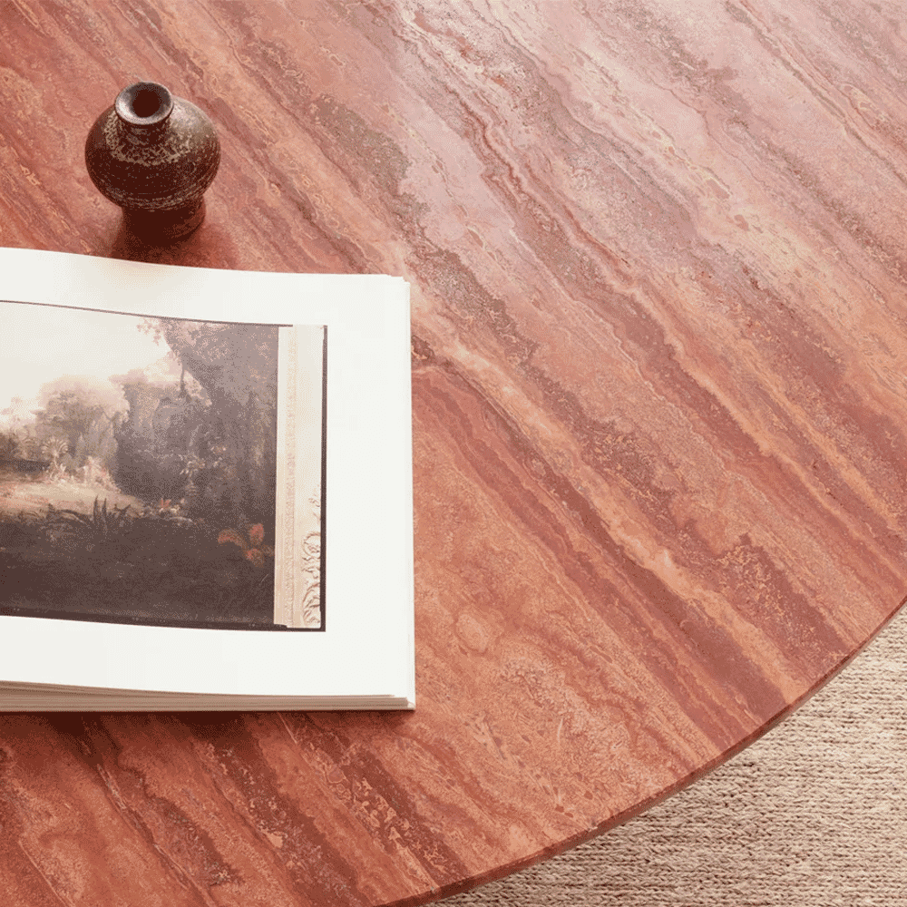 Close-up of a reddish marble tabletop with an open book and a small ceramic vase.