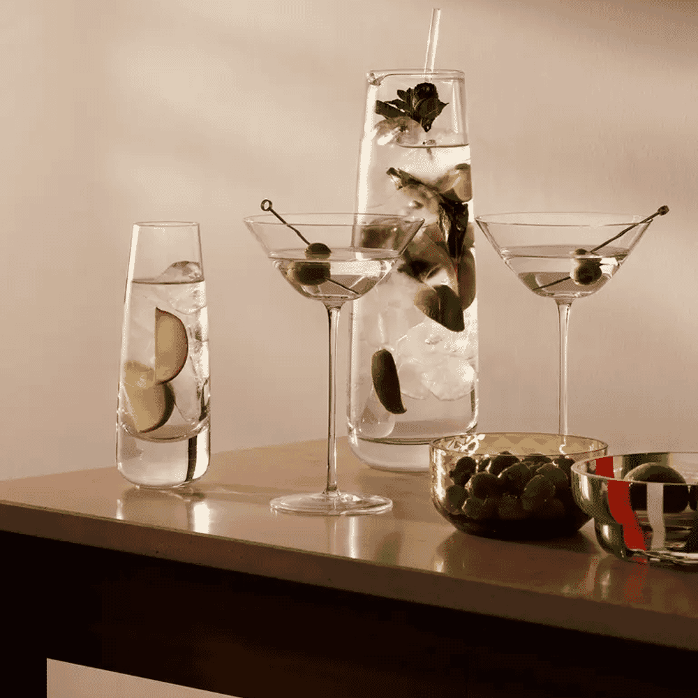 A sepia-toned arrangement of carafes, cocktail glasses, and garnishes on a bar surface.