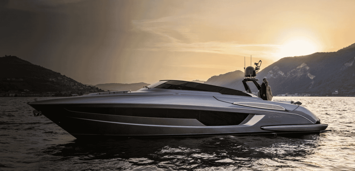 Man in a formal dark suit standing on the deck of a Riva yacht at sunset