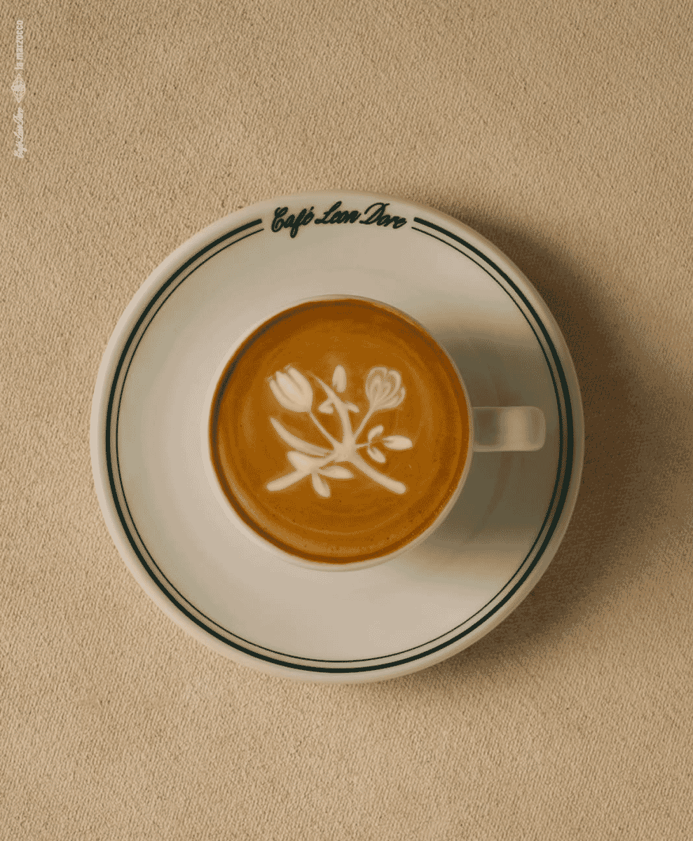 A cup of latte art featuring a floral design in a Café Leon Dore ceramic cup.
