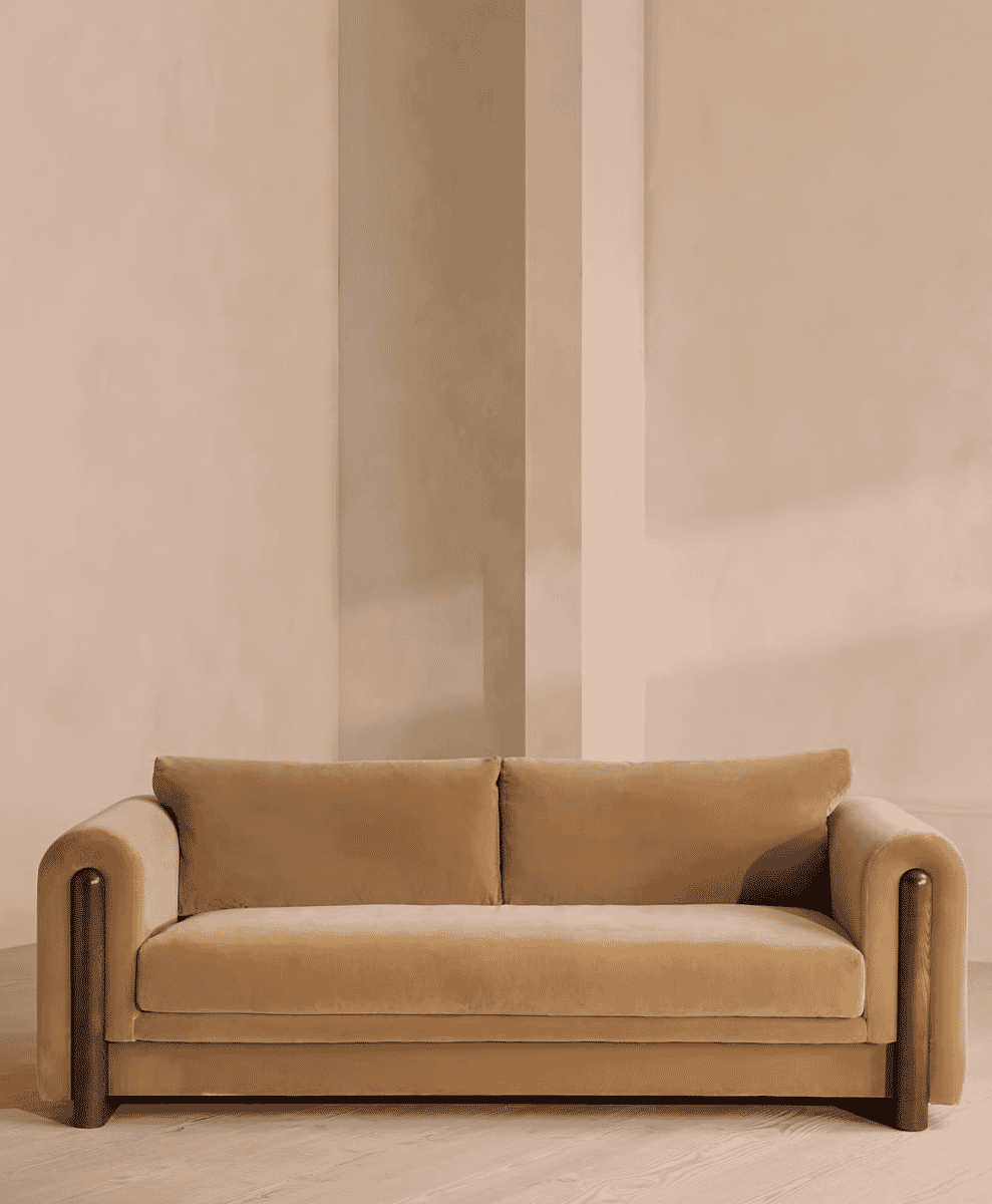 Beige velvet sofa with wooden armrests in a neutral-toned room.