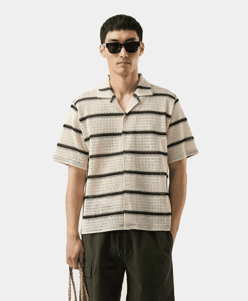 A man models a black-and-white vertically striped knitted short-sleeve shirt with dark pants.