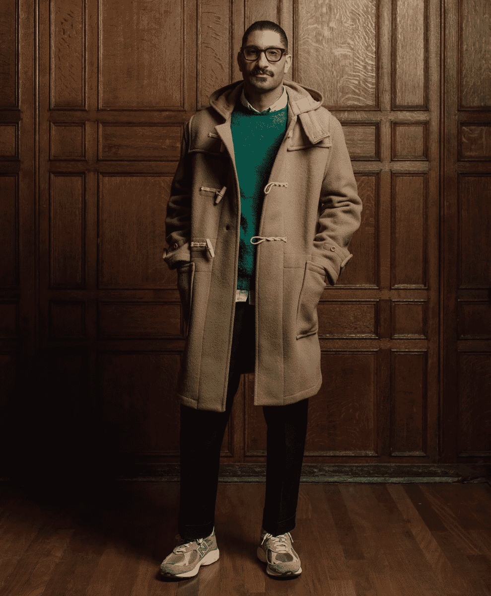 Man wearing a classic beige duffle coat with toggle fastenings over a teal sweater.