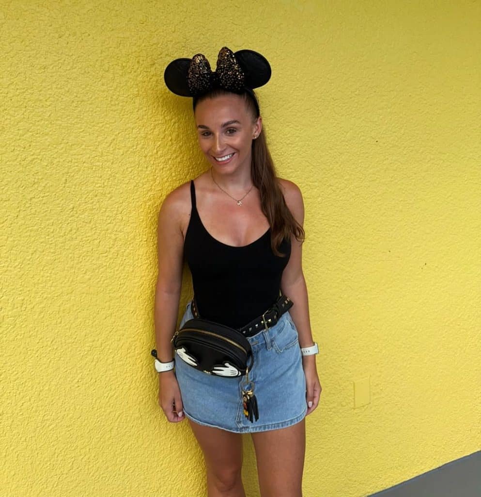 A close-up of a woman wearing a Mickey-themed fanny pack and denim skirt.