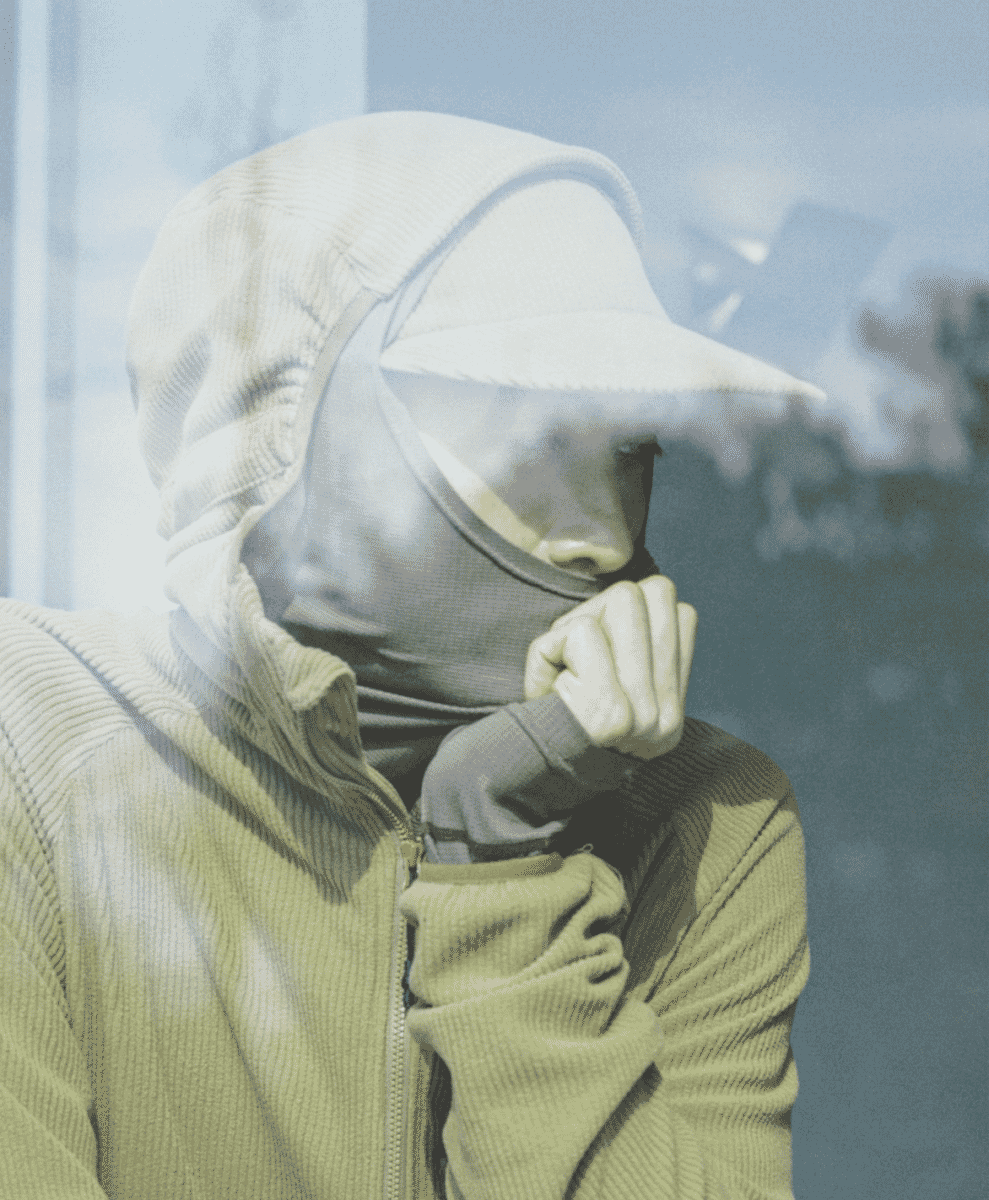 A person in a hooded corduroy jacket with a face mask in an indoor setting