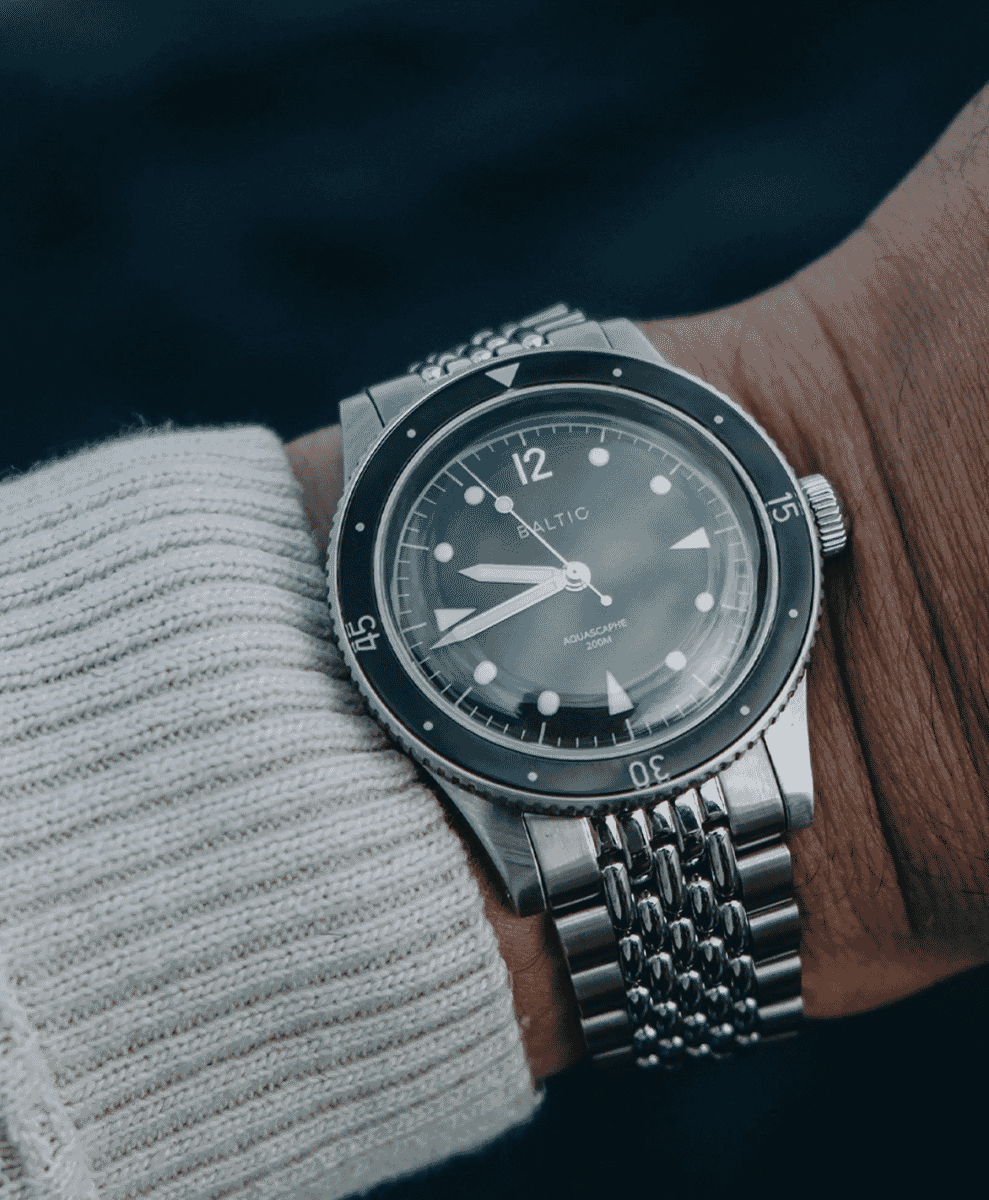 A person wearing a silver-tone Baltic Aquascaphe on the wrist, paired with a white ribbed sweater.