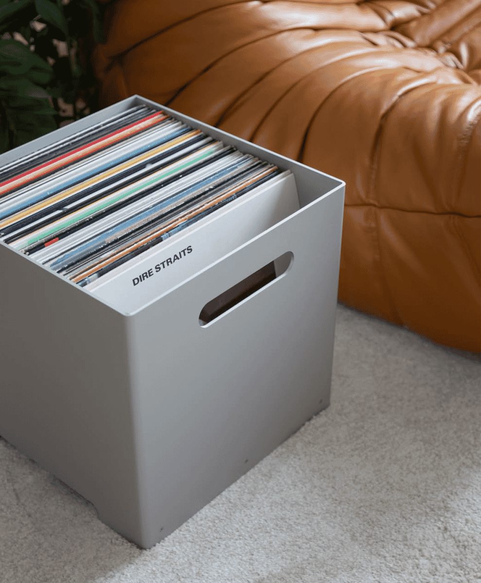 A gray vinyl record storage box labeled 'Dire Straits' beside a leather sofa.