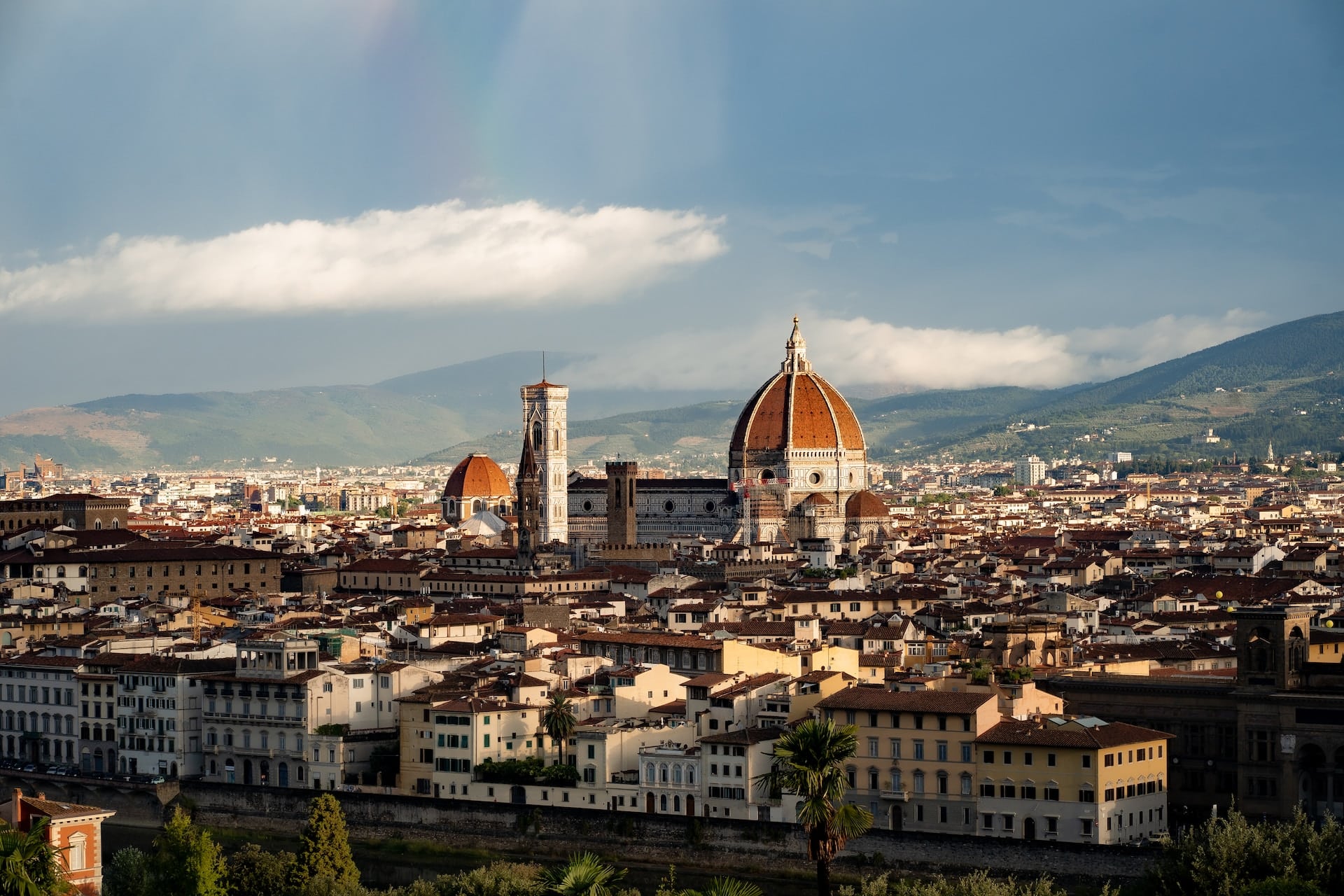 Panoramic view of Florence’s historic skyline with iconic domes and terracotta rooftops under a partly cloudy sky.