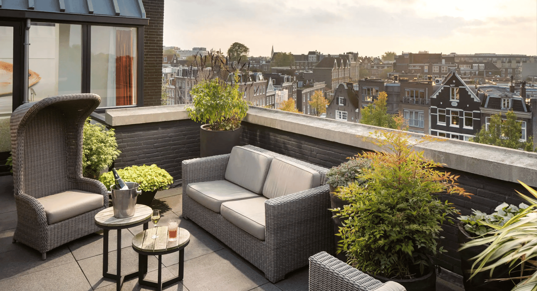 Stylish rooftop terrace with wicker furniture and panoramic city views at sunset.