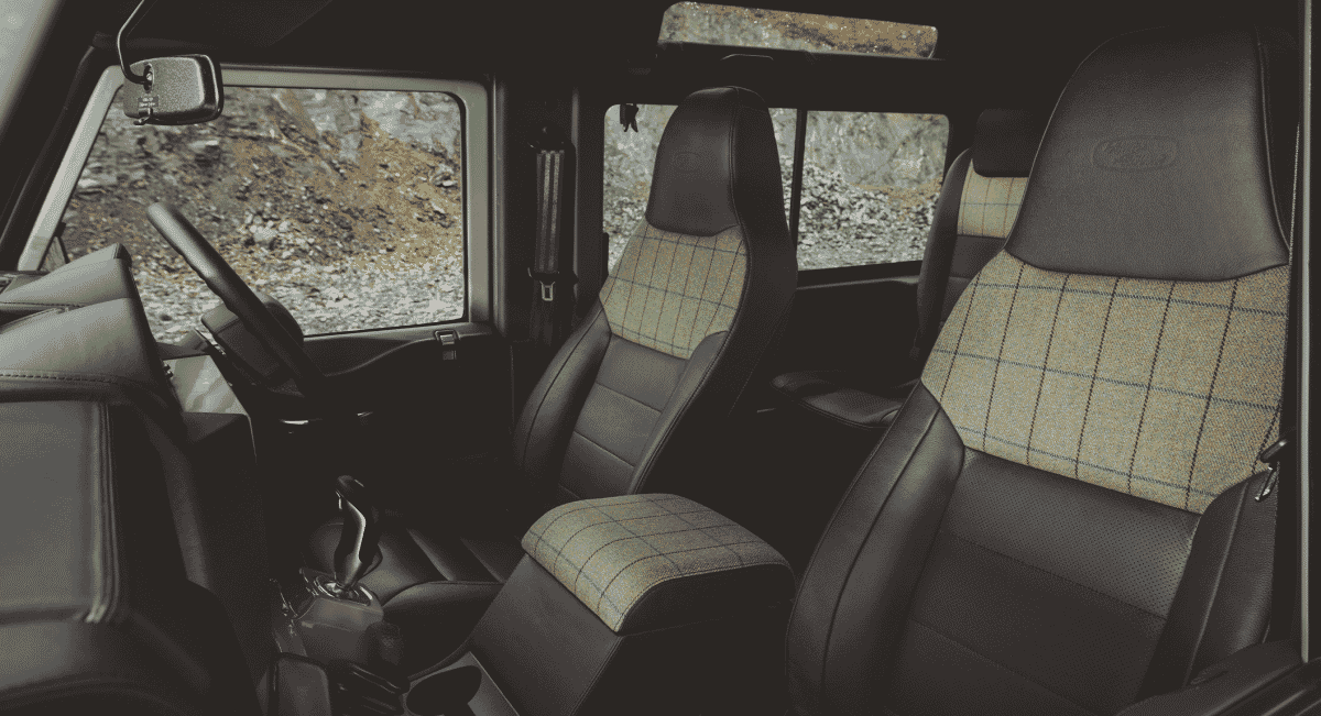 Close-up of Land Rover interior showing black leather seats with beige plaid fabric inserts.
