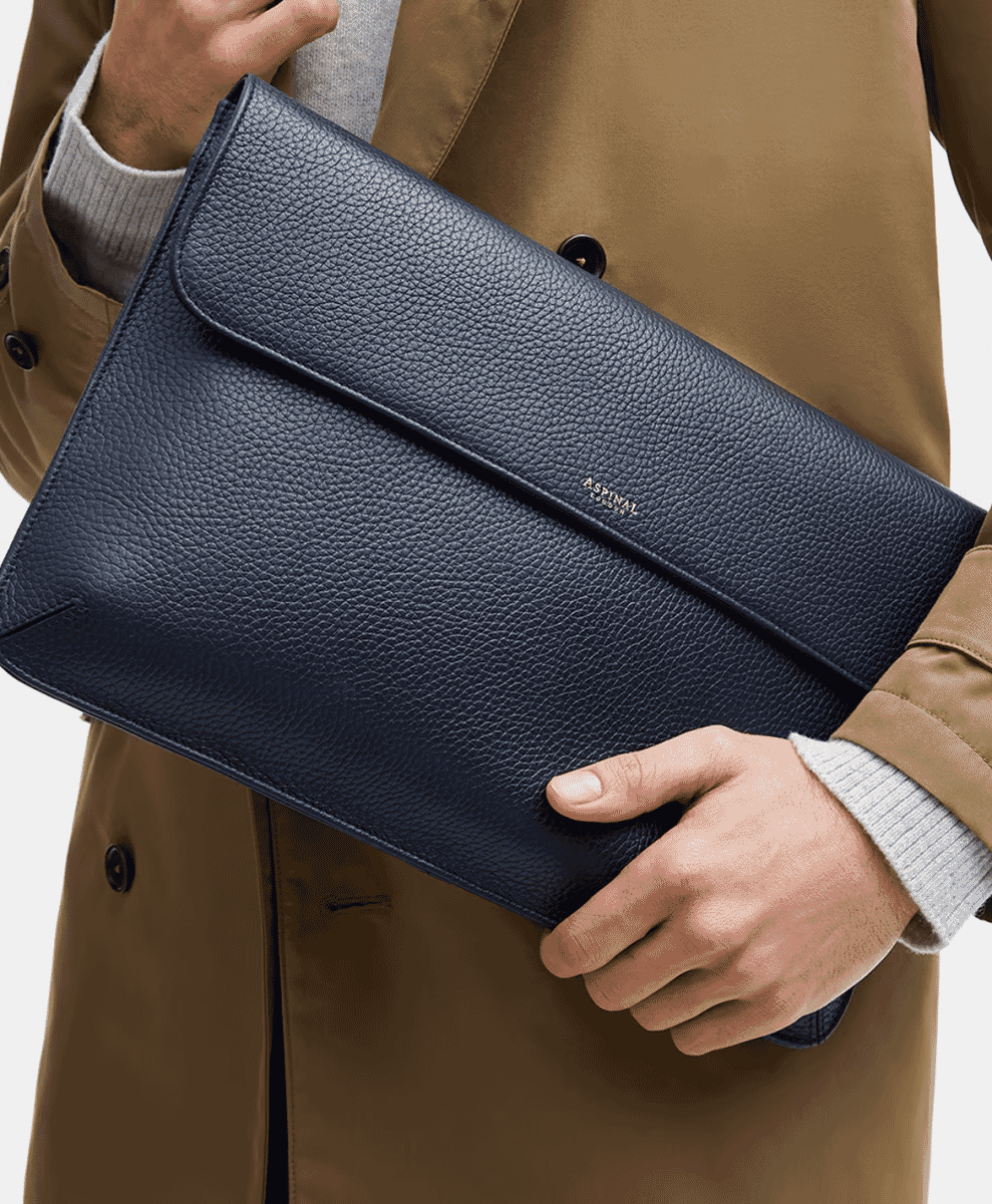 Close-up of a man's hand holding a navy blue leather sleeve against a tan coat.