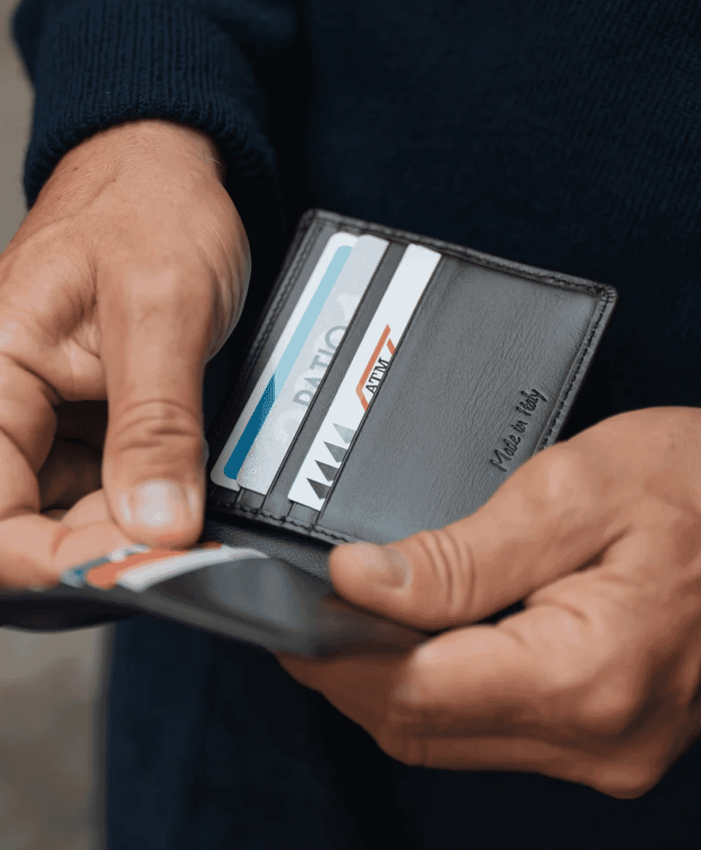 Hand holding a black leather cardholder embossed with 'Made in Italy'.
