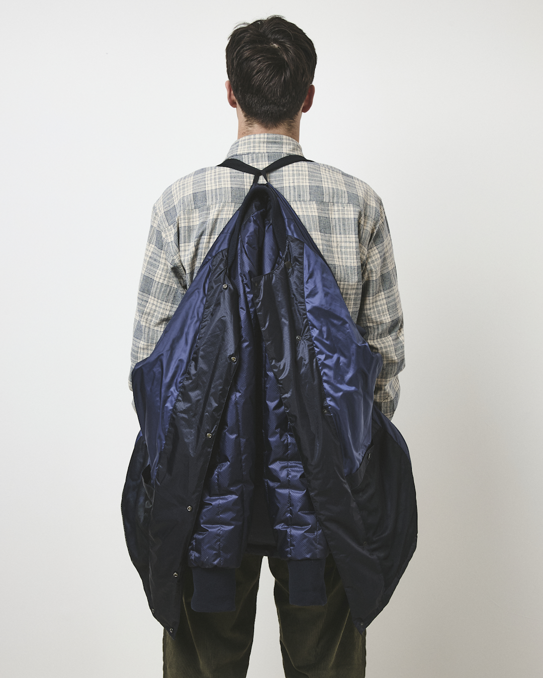 Back view of a man carrying a navy puffer jacket over his shoulders using integrated black straps.