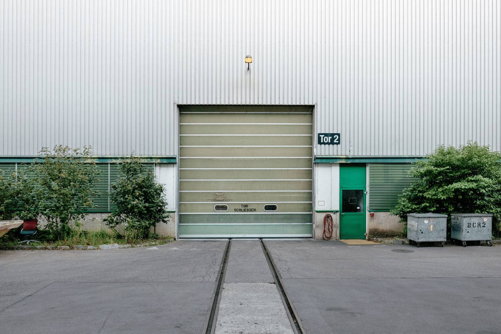 Industrial warehouse facade featuring a green roll-up door and concrete surroundings.