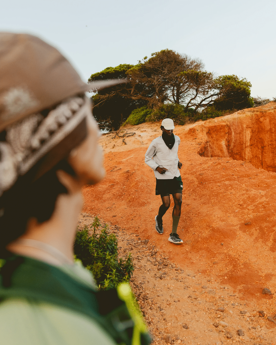 A runner in a white jacket and black shorts traversing a rugged red dirt trail.