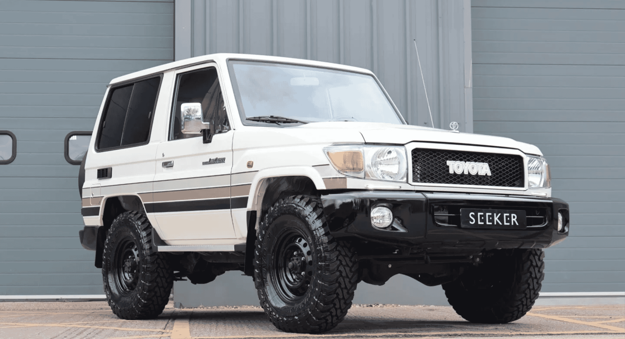 Full profile shot of a white Seeker UK Toyota Land Cruiser against an industrial gray backdrop.