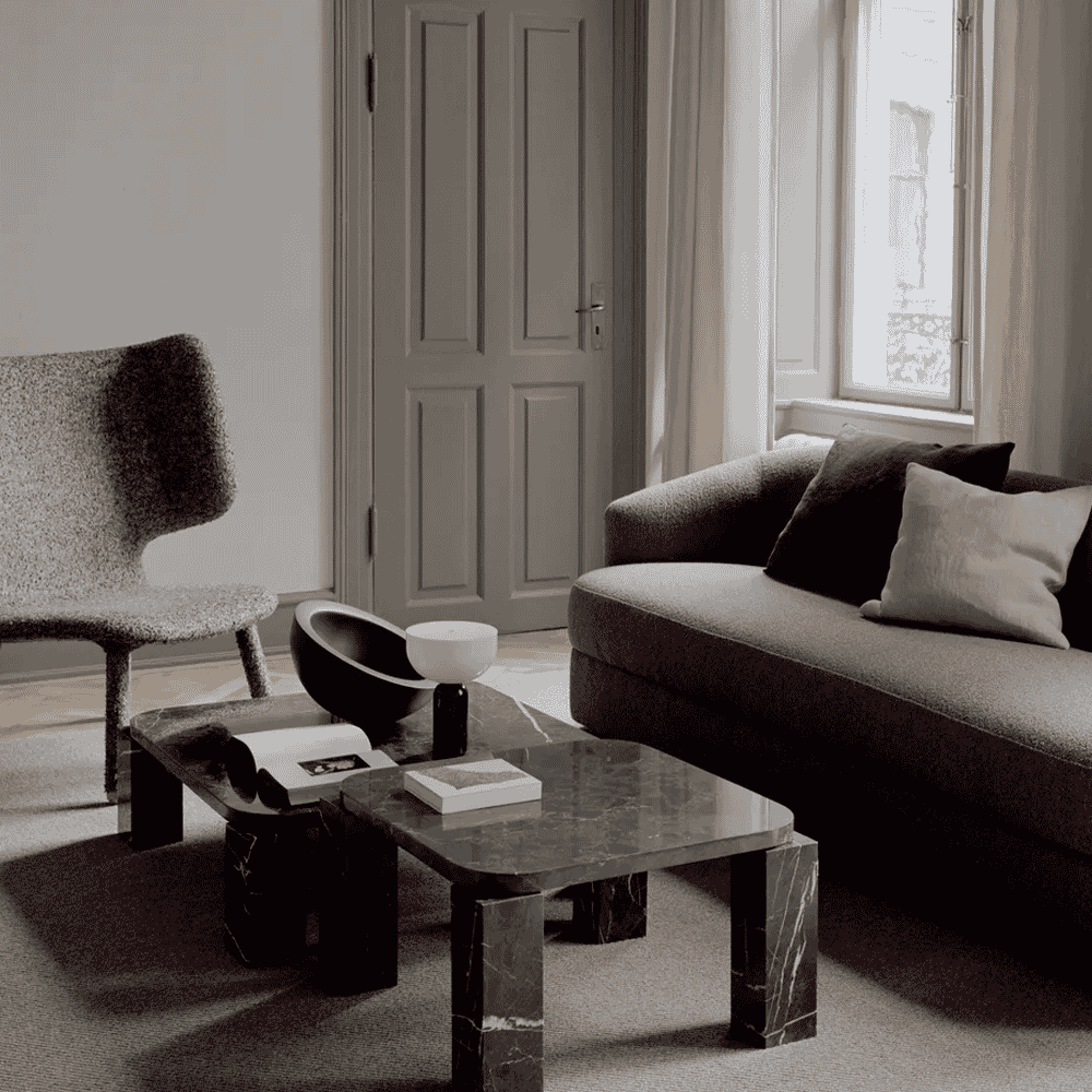 A low-slung marble coffee table placed on a textured rug in a minimalist living room.