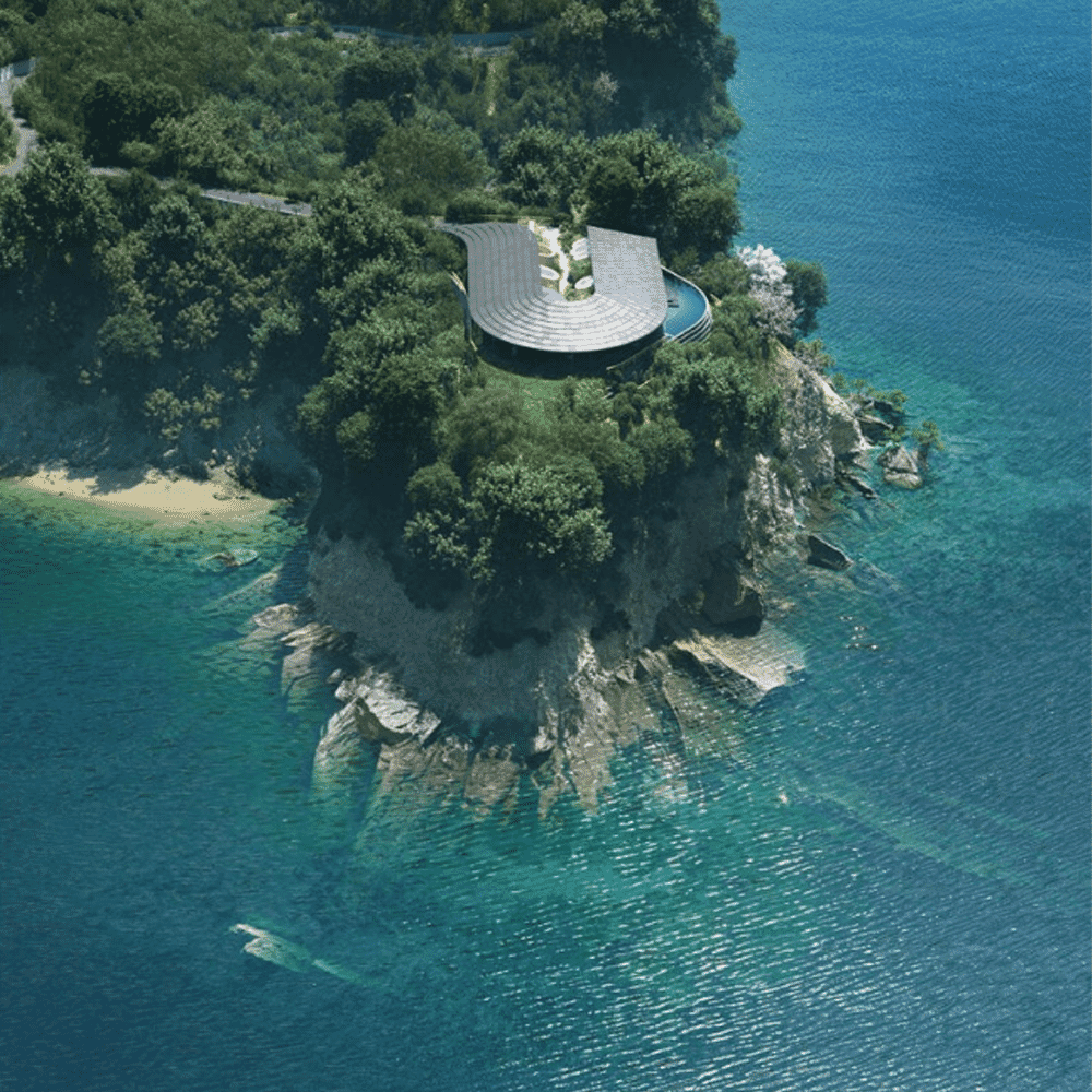 Wide aerial shot of the curved architectural structure blending into the lush greenery of a coastal cliff.
