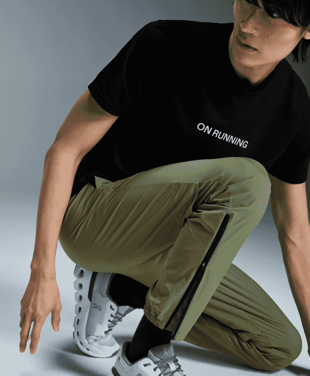 Male model in olive green athletic pants with side zippers and running shoes.