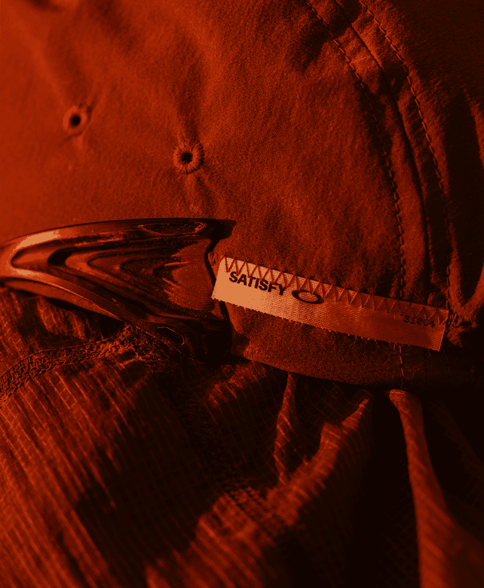 Close-up of a SATISFY and Oakley garment tag on textured fabric.