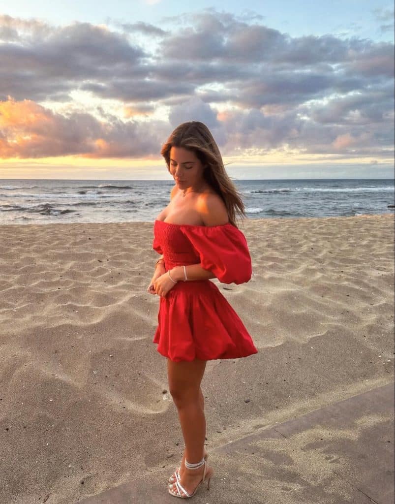 Woman in a vibrant red off-the-shoulder dress on a beach at sunset.