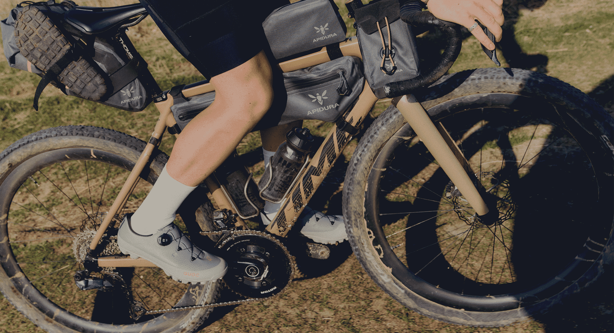 A gravel bike equipped with Apidura bags and a rider wearing grey QUOC shoes.