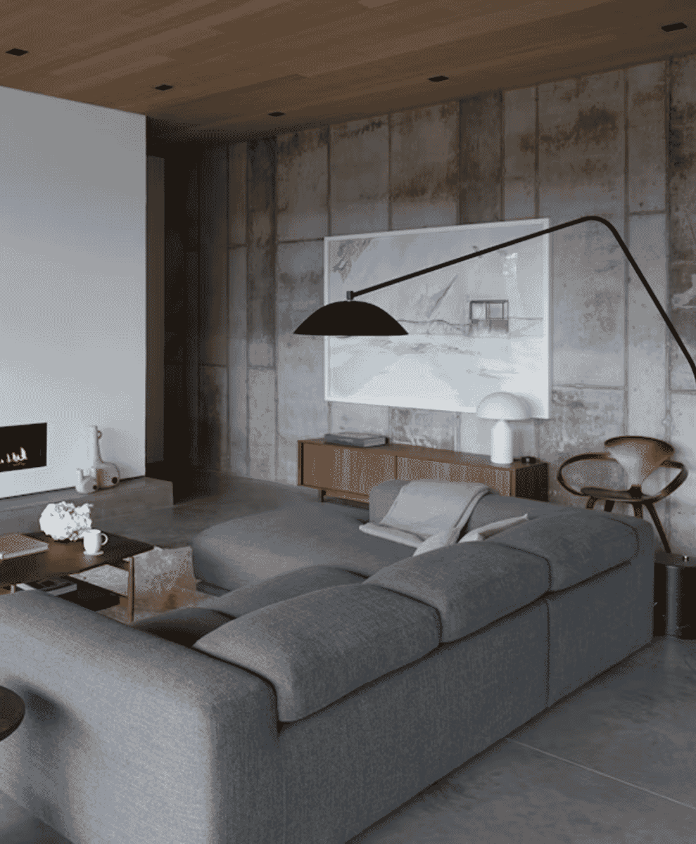 A modern living room with concrete walls, a large abstract painting, and a minimalist gray sectional sofa.