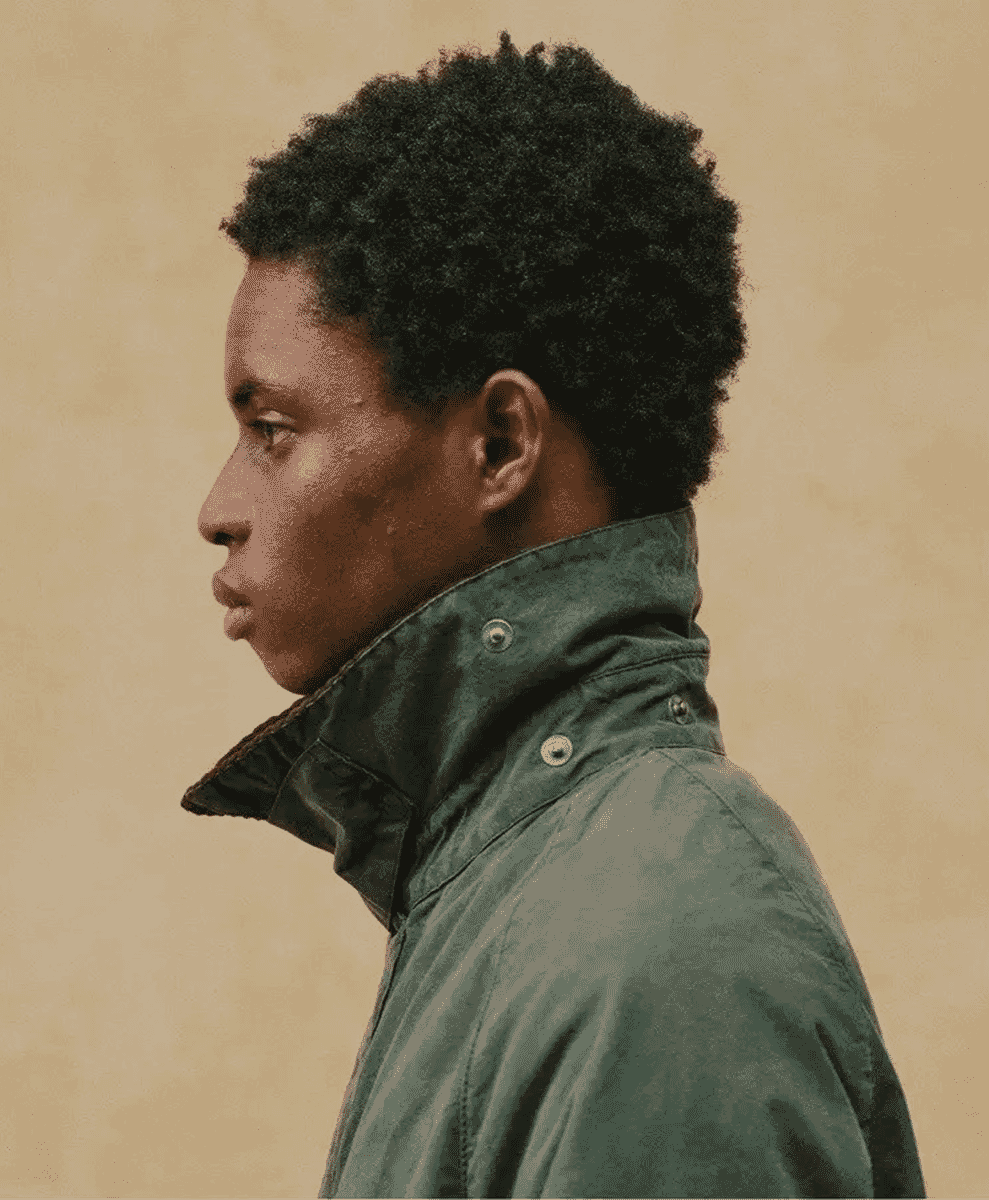 Profile shot of a man in a dark green high-collared jacket against a neutral beige background.
