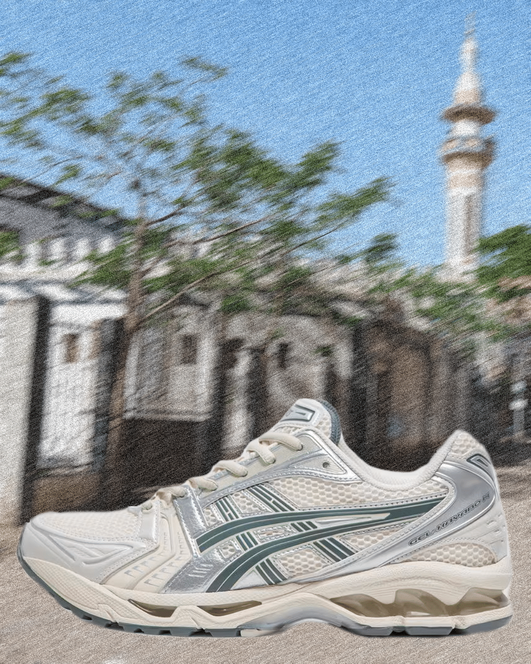 White and silver Asics Gel-Kayano 14 sneaker with green accents against an urban skyline.