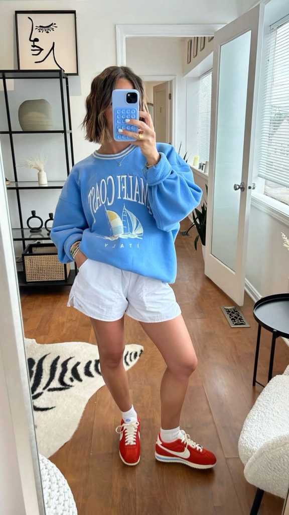 Woman in a blue Malibu Coast sweatshirt and red Nike sneakers.