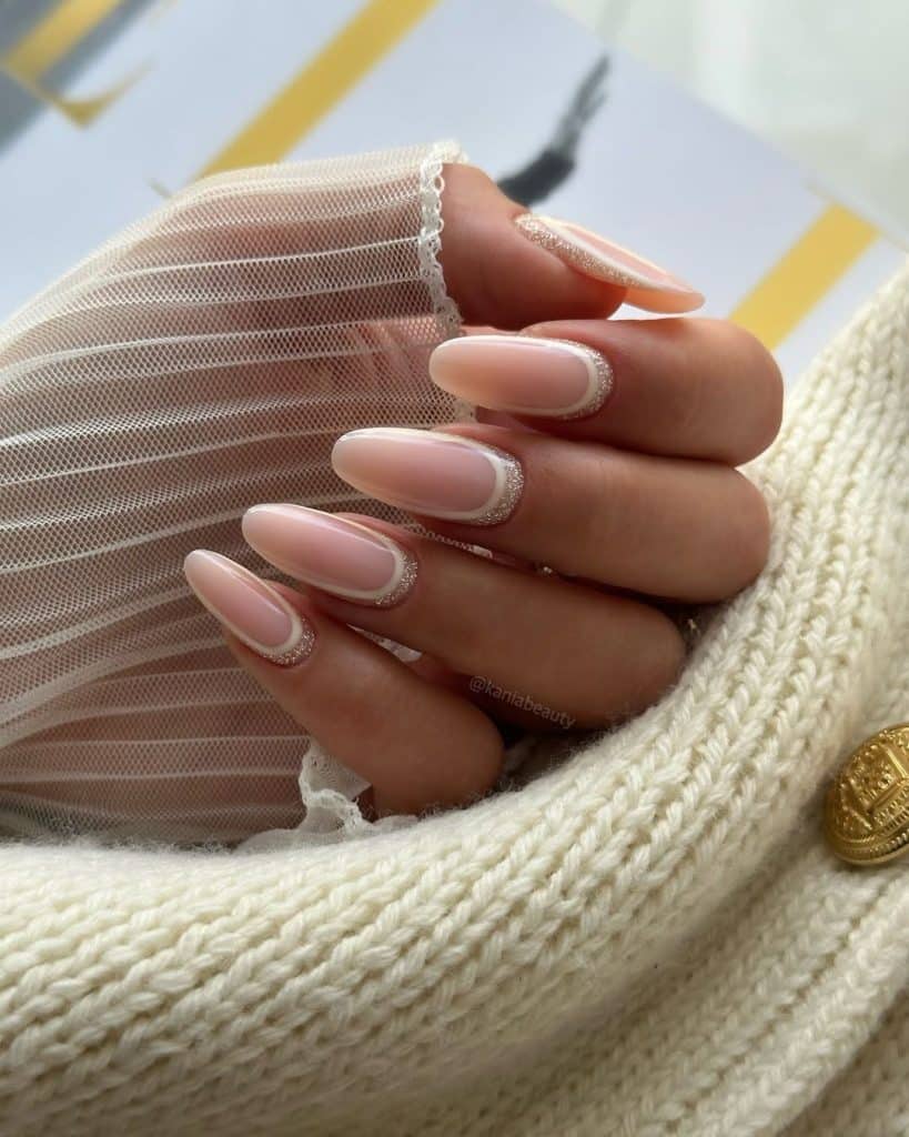 Nude French manicure with glitter accents resting on a cream knit.