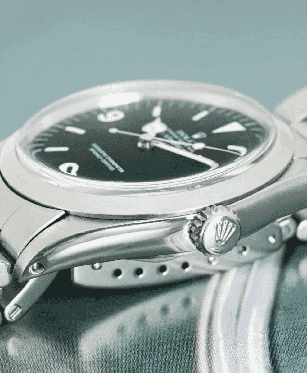 Rolex Explorer 1016 with a black dial and stainless steel bracelet on a textured background.