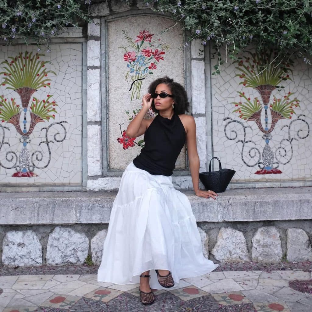 A woman in a black halter top and white midi skirt posing on a mosaic bench.