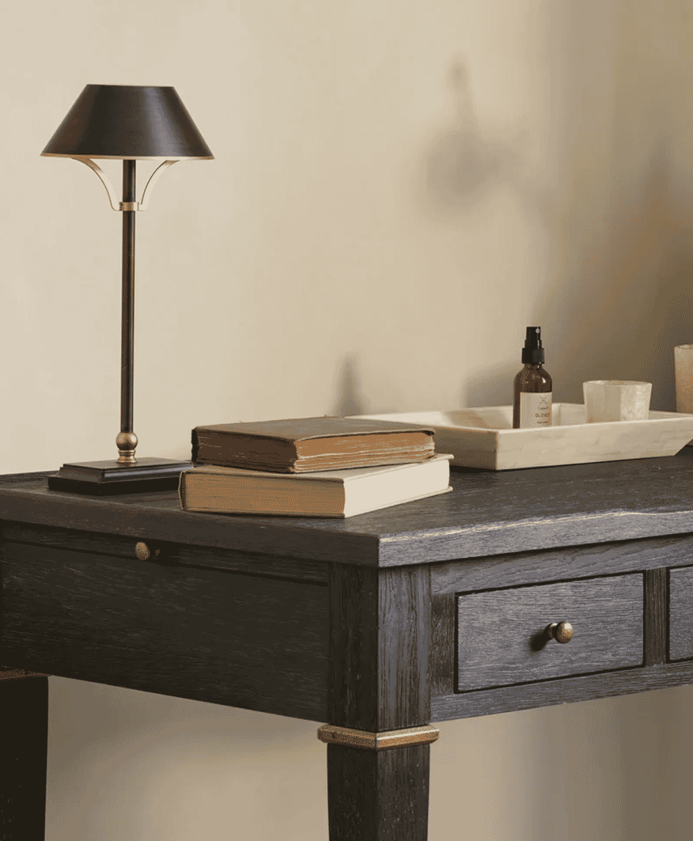 Dark wooden desk with a minimalist black lamp and organized book stack.