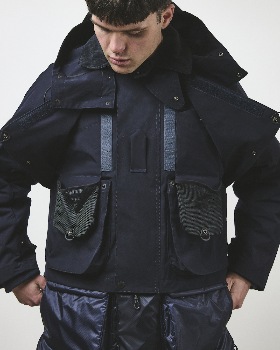 Man wearing a navy tactical jacket with multiple utility pockets and a high collar.