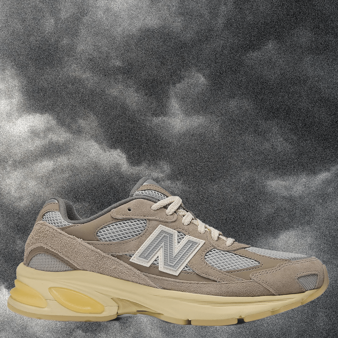 Beige and gray New Balance sneaker with mesh panels set against a dramatic grayscale cloud background.