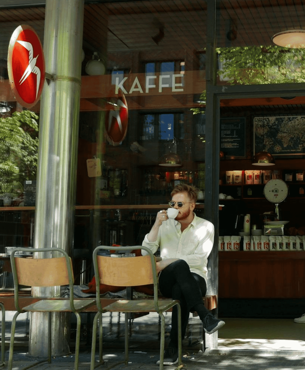A man in a crisp white button-up shirt sipping coffee at an outdoor café.