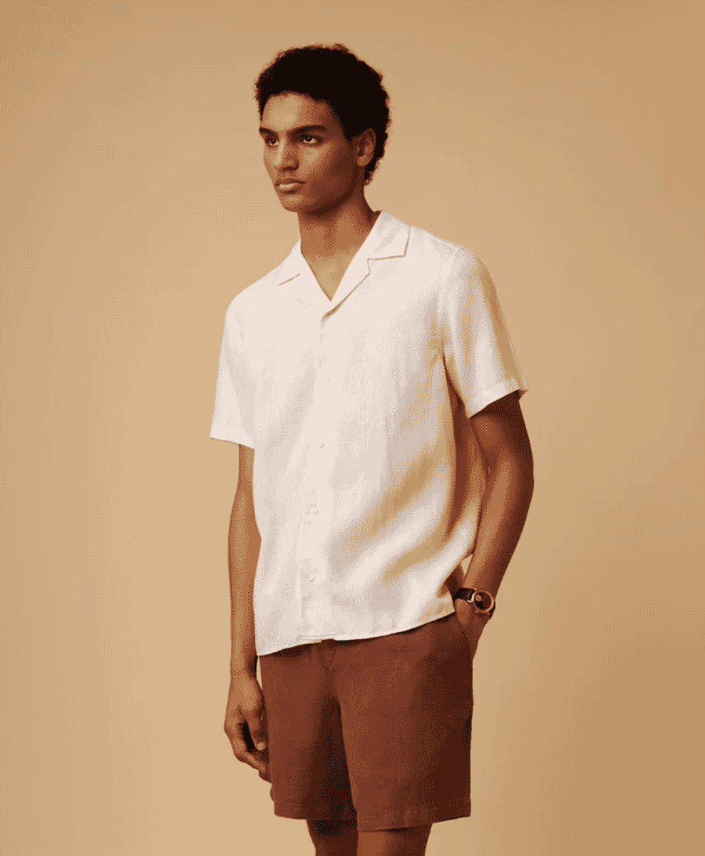 Man modeling a white short-sleeved camp-collar linen shirt against a beige background.