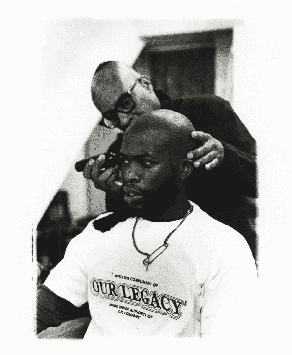 A man in an 'Our Legacy' branded graphic T-shirt in a barber shop environment.