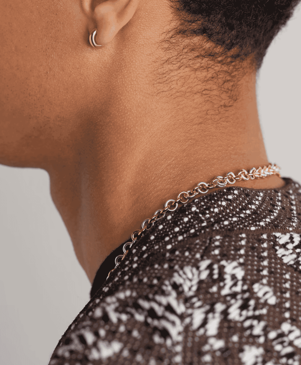Close-up of a person wearing a gold hoop earring paired with a gold and silver chain necklace.