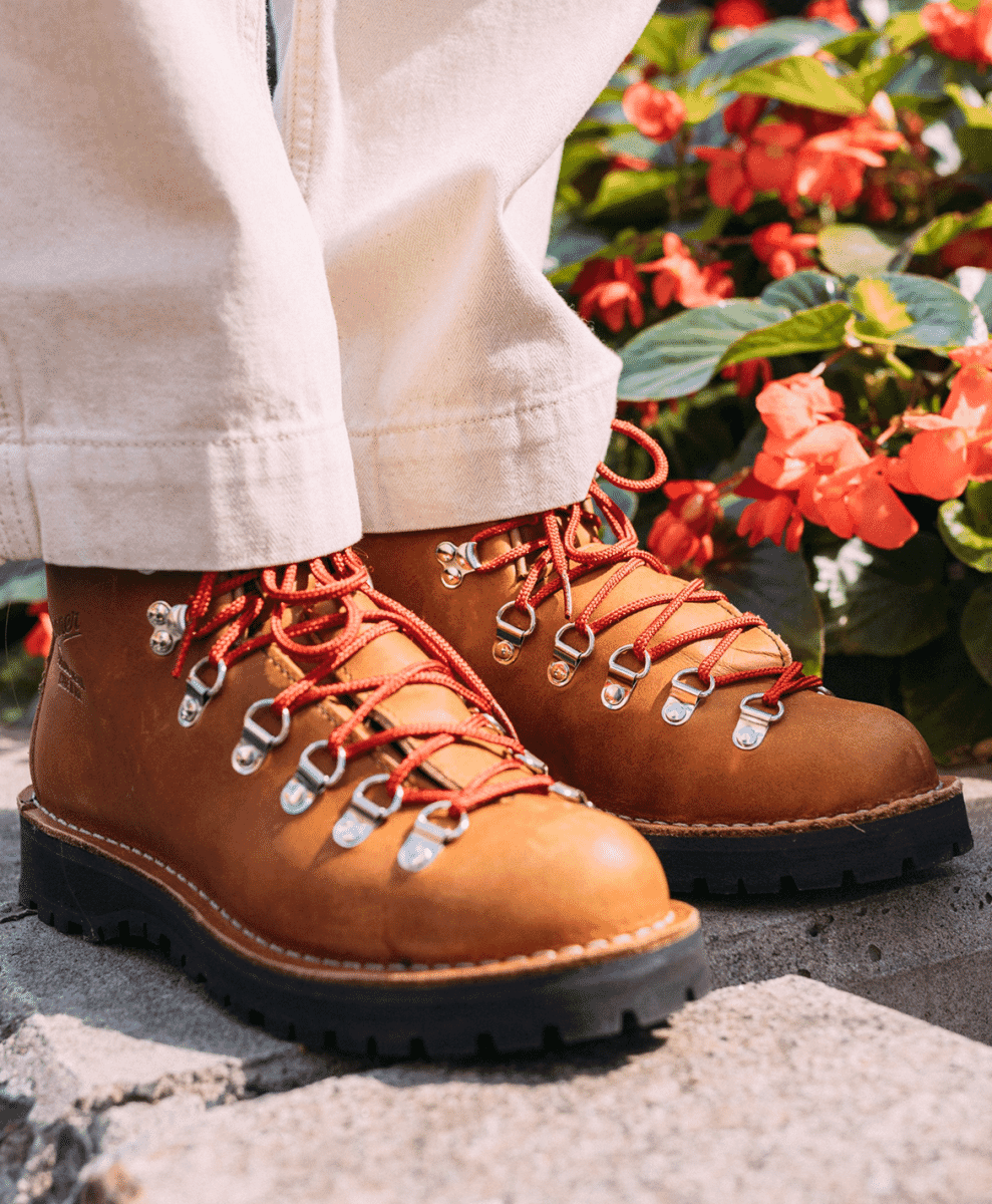 Close-up of tan leather hiking boots with vibrant red laces on weathered stone steps next to orange flowers.