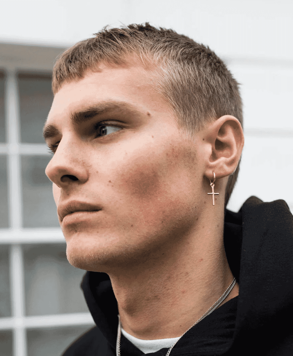 A man in a black hoodie wearing a small cross earring in a street setting.