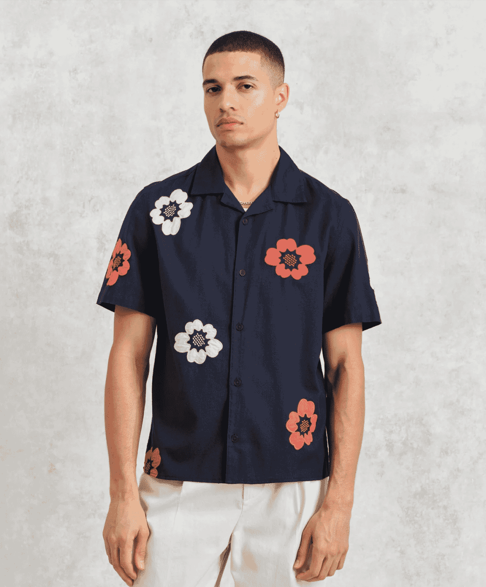 A man wearing a navy button-up shirt with colorful floral 3D appliqués.
