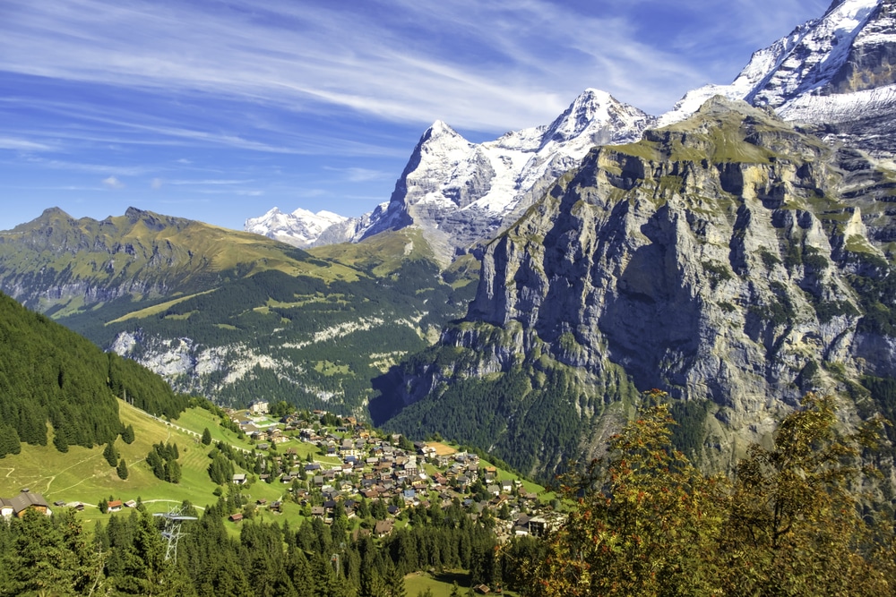A picturesque alpine village with wooden chalets set against a backdrop of snow-capped mountain peaks.