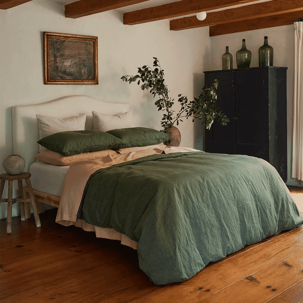 Earthy green linen bedding on a bed with a wooden beam ceiling in a rustic room.